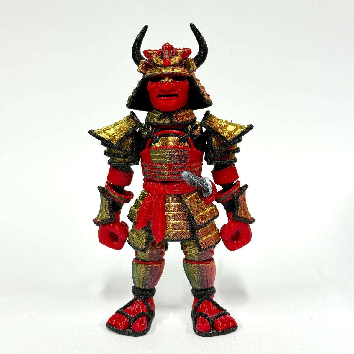 A red and gold Japanese samurai action figure with black horns on its helmet, standing against a plain white background.